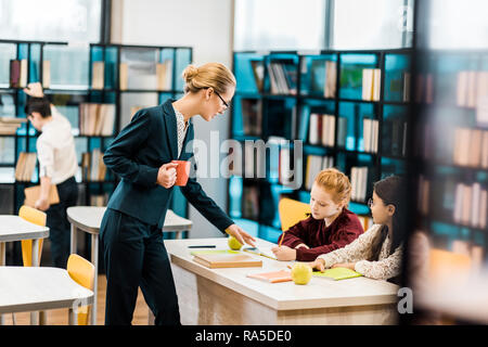 Jeune enseignante holding cup et à la bibliothèque à étudier en écolières Banque D'Images