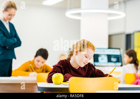 À l'enseignant à l'adorable élèves à étudier et à écrire à un bureau Banque D'Images