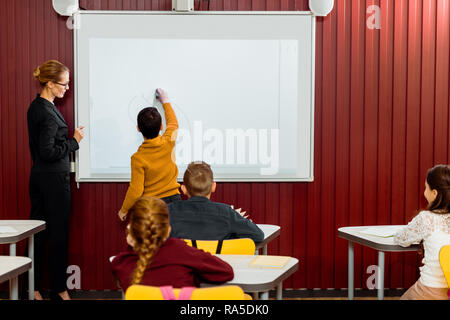 Vue arrière de l'écriture sur tableau blanc interactif garçon pendant la leçon Banque D'Images