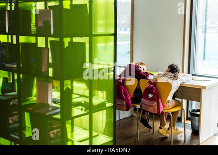 Vue arrière de l'ennuyer ecolières lying on table in library Banque D'Images