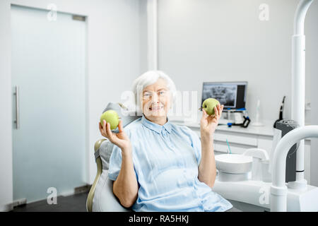 Portrait d'un beau sourire en santé senior woman holding green apple au cabinet dentaire Banque D'Images