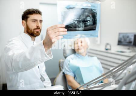 Aîné heureux femme durant la consultation avec beau dentiste montrant une radiographie panoramique dans le cabinet dentaire Banque D'Images