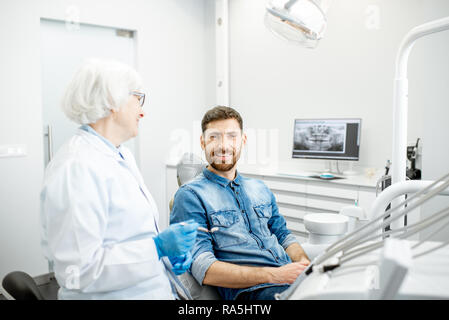 Portrait of a handsome male patient in blue shirt avec femme âgée dentiste dans le cabinet dentaire Banque D'Images