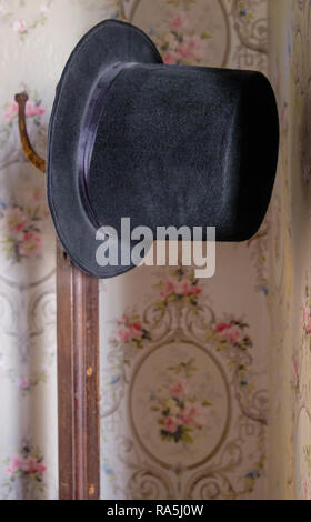 Vintage noir top hat sur hat stand. Papier peint rétro floral en arrière-plan. Intérieur de l'ancien accueil Texan, Chestnut Square McKinney au Texas. Banque D'Images