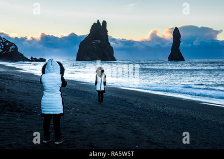 Les touristes sur la plage de sable noir de Reynisfjara qui jouit dans la lumière du matin, avec des vagues de l'océan Atlantique en roulant au-delà de la mer de Reynisdrangar stacks, Islande [Pas de m Banque D'Images