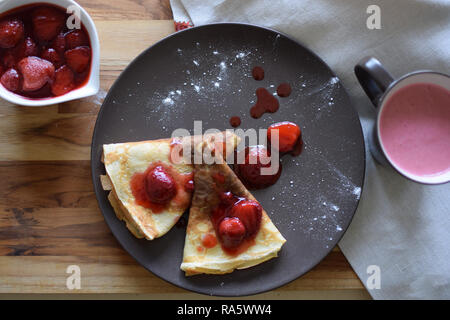 Crêpes maison avec du fromage cottage et les fraises dans une assiette. Fond de bois. Banque D'Images