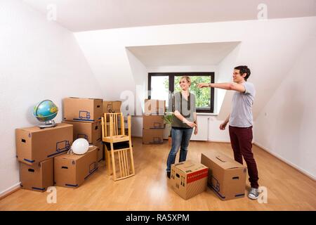 Jeune couple transportant des cartons et des meubles dans la salle vide d'un appartement loft Banque D'Images