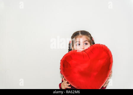 Jolie petite fille adorable en forme de cœur rouge détient balloon.Maison de vacances isolée avec concept background Banque D'Images