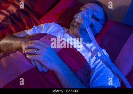 L'homme avec l'apnée du sommeil, porte un masque CPAP pendant le sommeil, masque respiratoire, qui pousse l'air dans les voies respiratoires en raison Banque D'Images