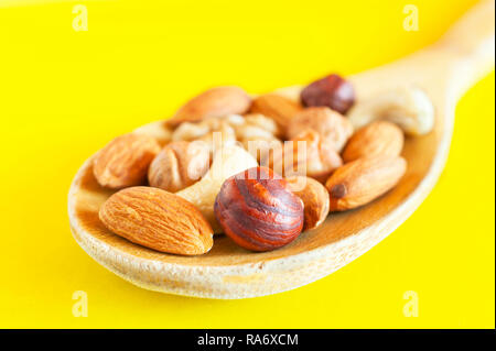 Amandes, noisettes, noix, noix de cajou dans une cuillère en bois isolé sur fond jaune. Le petit-déjeuner, collation biologiques sains, les ingrédients alimentaires. Banque D'Images