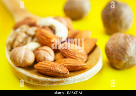 Amandes, noisettes, noix, noix de cajou dans une cuillère en bois, et trois Noix entière isolé sur fond jaune. Le petit-déjeuner, collation biologiques sains, F Banque D'Images