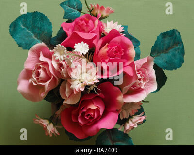Bouquet de fleurs artificielles roses rose et vert feuilles vu de dessus avec un fond vert Banque D'Images