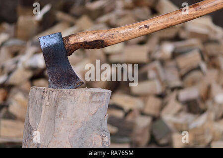 Close up d'une hache dans un bloc de bois avec une pile de grumes dans l'arrière-plan Banque D'Images