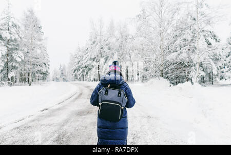 Style de voyage. Jeune femme avec sac à dos à l'hiver à marcher le long de la route enneigée en Suède Banque D'Images