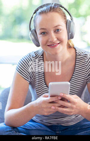 Portrait de femme à la maison de la musique en continu à partir d'un téléphone portable sur un casque sans fil Banque D'Images