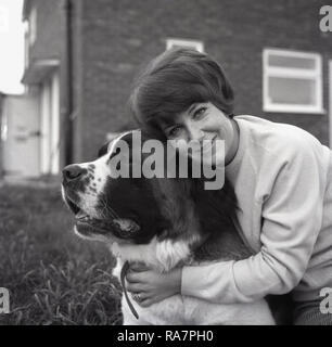 1967, femme tenant affectueusement son gros chien, un St Bernard, England, UK. Cette grande race de chien vient de Suisse ou d'Italie et ont été à l'origine la race pour le sauvetage en montagne par l'hospice du Grand St Bernard pass sur la frontière italo-suisse. Banque D'Images