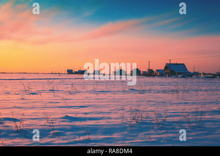 Paysage rural en hiver. Le champ couvert de neige et de rangée de maisons à l'horizon au coucher du soleil Banque D'Images