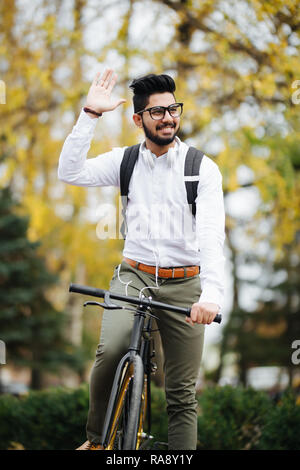 Handsome businessman occasionnels aller au travail en vélo. Il est riding bike et forme Bonjour. Banque D'Images