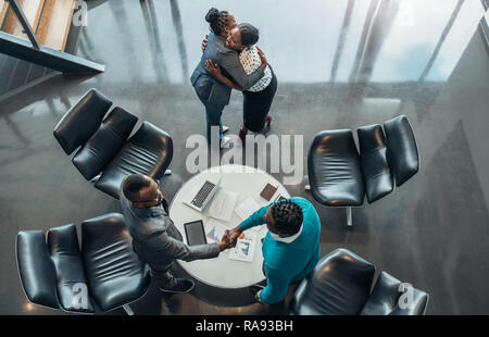 Des collègues africains et message d'abord remercier chacun d'autres après le succès de la réunion. Deux femme sont hugging et deux hommes sont shaking hands Banque D'Images