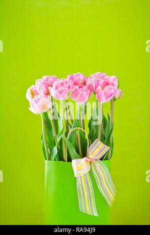 Bouquet de tulipes roses dans un vase avec un nœud papillon multicolore sur un fond vert clair, de copie ou de l'espace texte Banque D'Images