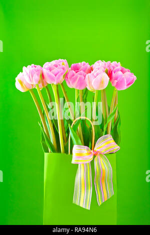 Bouquet de tulipes roses dans un vase avec un nœud papillon multicolore sur un fond vert vif au printemps, modèle pour les fleuristes Banque D'Images