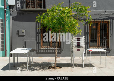 Un arbre vert à côté de tables de restaurant et des chaises sur le street​ à Denia, Espagne. Banque D'Images