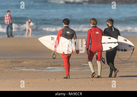 Leurs Surfers carrying surfboards, marcher sur la plage de Fistral vers la mer. Banque D'Images