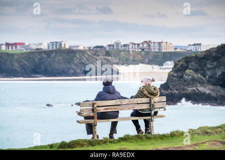 Des gens assis sur un banc sur la côte donnant sur la mer à Newquay en Cornouailles. Banque D'Images