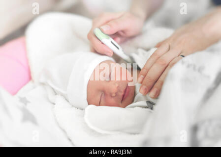 Bébé dans le lit mesure la température du corps. Maman mesure la température du corps du bébé avec un thermomètre. Banque D'Images