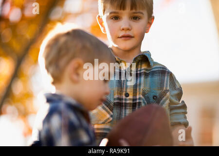 Portrait de garçon debout à côté de son petit frère avec le ballon de rugby. Banque D'Images