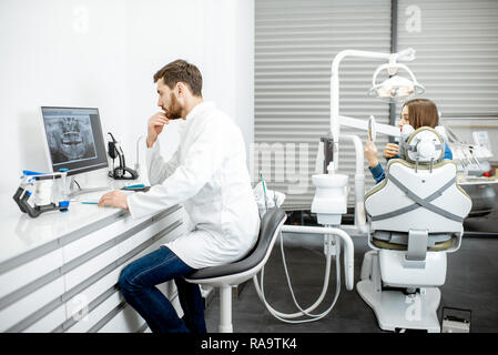 Dentiste travailler avec ordinateur dans le cabinet dentaire avec femme patient sur l'arrière-plan Banque D'Images