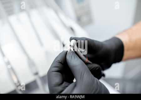 Close-up d'une fraise dentaire avec l'injecteur dans les mains en noir gants médicaux Banque D'Images