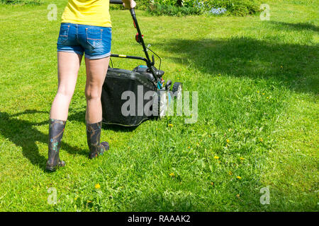 Belle fille coupe la pelouse tondre le gazon Tondeuse sur l'herbe verte de l'herbe de tonte tondeuse matériel outil de travail soins jardinier vue en gros journée ensoleillée Banque D'Images