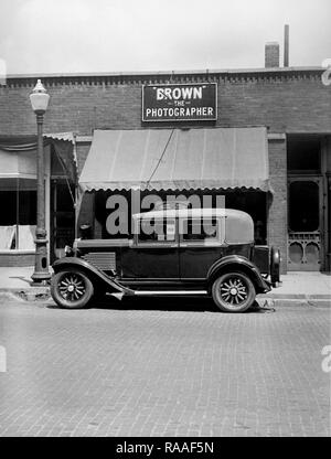 Période d'une voiture est garée dans la rue en face d'un studio de photographes, ca. L'année 1930. Banque D'Images