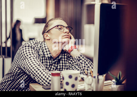 Bored young man leaning on sa table Banque D'Images