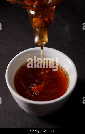 Le processus d'infusion de thé. Cérémonie du thé, une tasse de boisson rose musqué fraîchement préparé, l'humeur sombre. On verse de l'eau chaude de la bouilloire dans la tasse avec le Banque D'Images