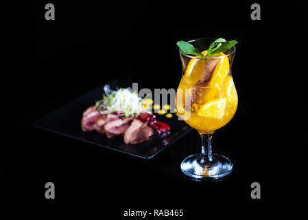 Verre d'hiver avec des morceaux d'orange et d'épices sur un fond noir. Banque D'Images