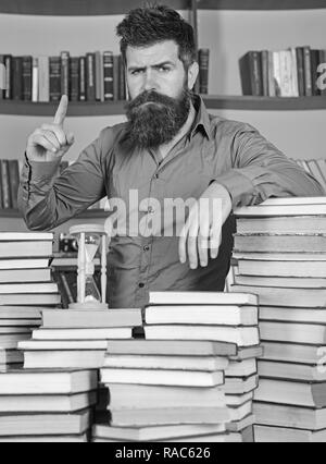 L'homme sur certain visage se tient entre des piles de livres, tout en étudiant en bibliothèque, des étagères sur l'arrière-plan. Enseignant ou étudiant avec barbe est à table avec des livres, des flous artistiques. Concept bibliothécaire. Banque D'Images