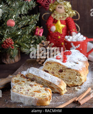 Stollen, un gâteau traditionnel européen avec les noix et fruits confits, est saupoudré de sucre glace et couper en morceaux sur une planche en bois brun Banque D'Images