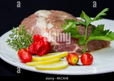La viande de buffle crus crus prêts à cuire dans une plaque blanche avec des tomates, du citron et des herbes d'un fond noir. Banque D'Images