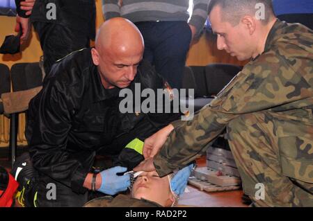 Un pompier medic et mettre de pansement sur une victime simulée's Head, à l'école primaire 59, lors d'une formation de premiers soins de base avec des soldats affectés à l'équipe de combat de la 3e Brigade blindée, 4e Division d'infanterie, 27 janvier 2017, à Zagan, Pologne. La brigade est ici que la première rotation de brigades blindées en Europe en faveur de la résolution de l'Atlantique. Cette rotation permettra d'améliorer les capacités de dissuasion dans la région, améliorer la capacité de répondre aux crises potentielles et défendre les alliés et partenaires de la Communauté européenne. Les forces américaines se concentrera sur le renforcement Banque D'Images