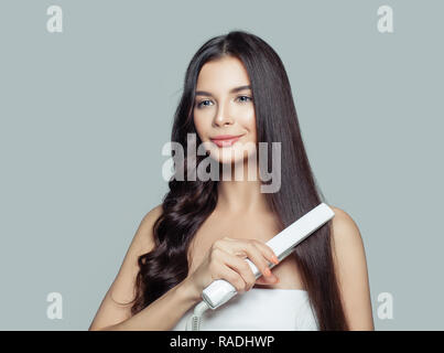 Belle femme avec de longs cheveux raides et des cheveux bouclés en utilisant Hair Straightener. Cute smiling girl brune sain de redressage hairstyle avec télévision je Banque D'Images