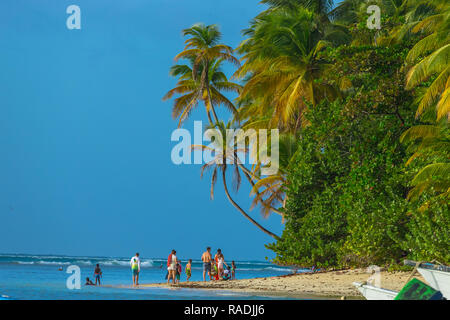 Pigeon Point, Tobago, les Caraïbes. La famille ou le groupe de personnes, se promener le long de la plage avec palmiers, ciel bleu et mer bleue. Paysage Banque D'Images