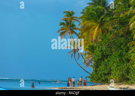 Pigeon Point, Tobago, les Caraïbes. La famille ou le groupe de personnes, se promener le long de la plage avec palmiers, ciel bleu et mer bleue. Paysage Banque D'Images