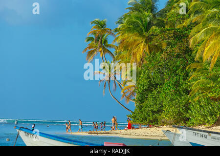 Pigeon Point, Tobago, les Caraïbes. La famille ou le groupe de personnes, se promener le long de la plage avec palmiers, ciel bleu et mer bleue. Paysage Banque D'Images