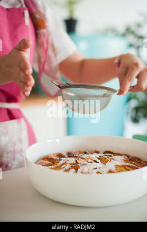Verser le sucre en poudre sur la tarte aux pommes faite maison. Femme au foyer de cuisiniers dans la cuisine Banque D'Images