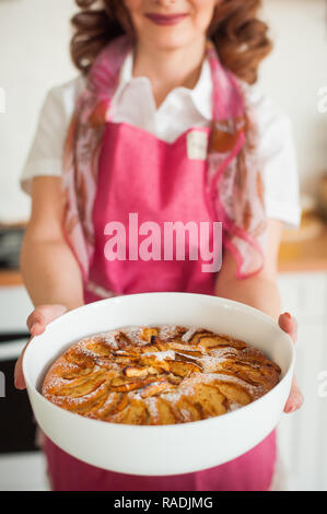 Jeune fille dans un tablier rose est titulaire d'une tarte aux pommes. Des gâteaux en forme de céramique Banque D'Images
