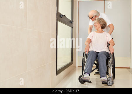 Homme pousse sa femme dans un fauteuil roulant dans la maison de retraite ou une clinique de réadaptation Banque D'Images