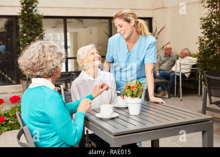 Assistant de soins infirmiers dans la conversation avec les femmes âgées à boire du café dans une maison de retraite Banque D'Images