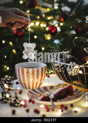 Boire le thé avec un gâteau à côté de l'arbre de Noël Banque D'Images